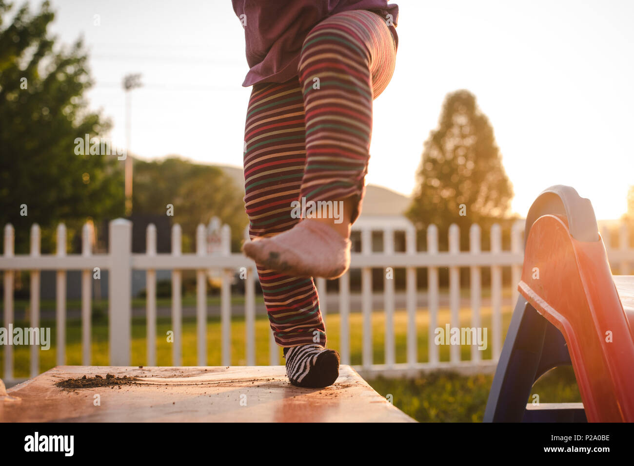 A little girl wearing striped pants and dancing on a slide. Stock Photo