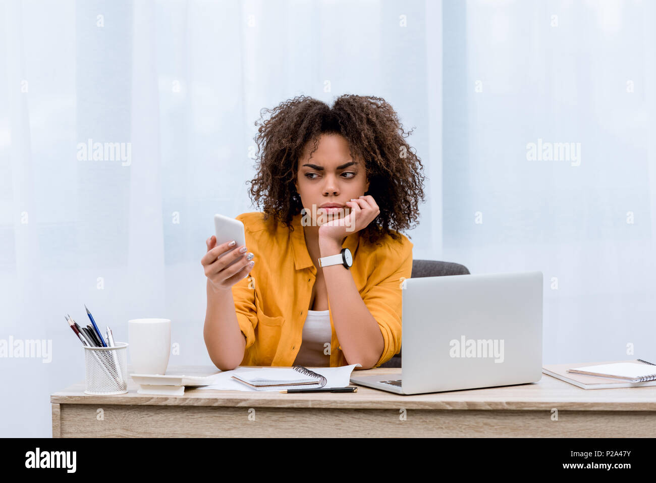 suspecting young woman looking at smartphone at workplace Stock Photo