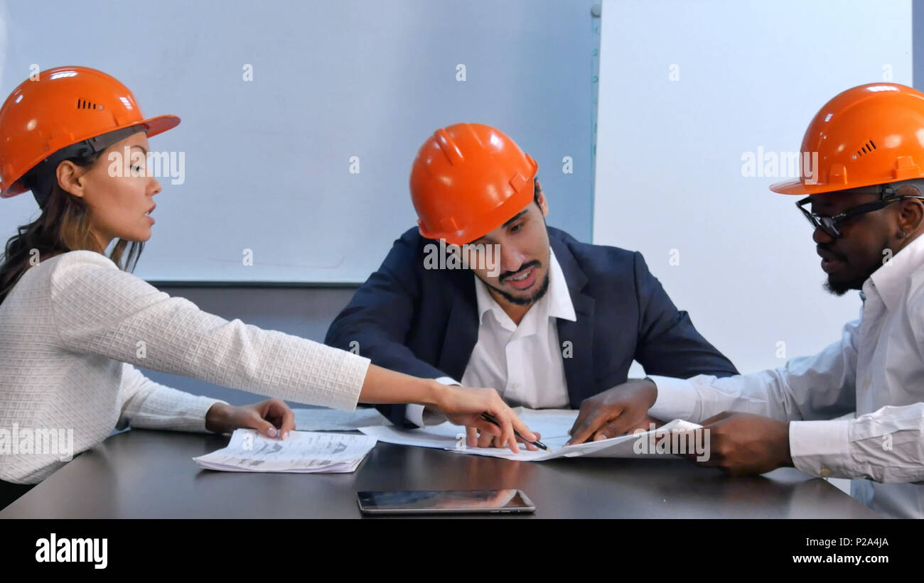 Multiracial colleagues reading construction documents, discussing it Stock Photo
