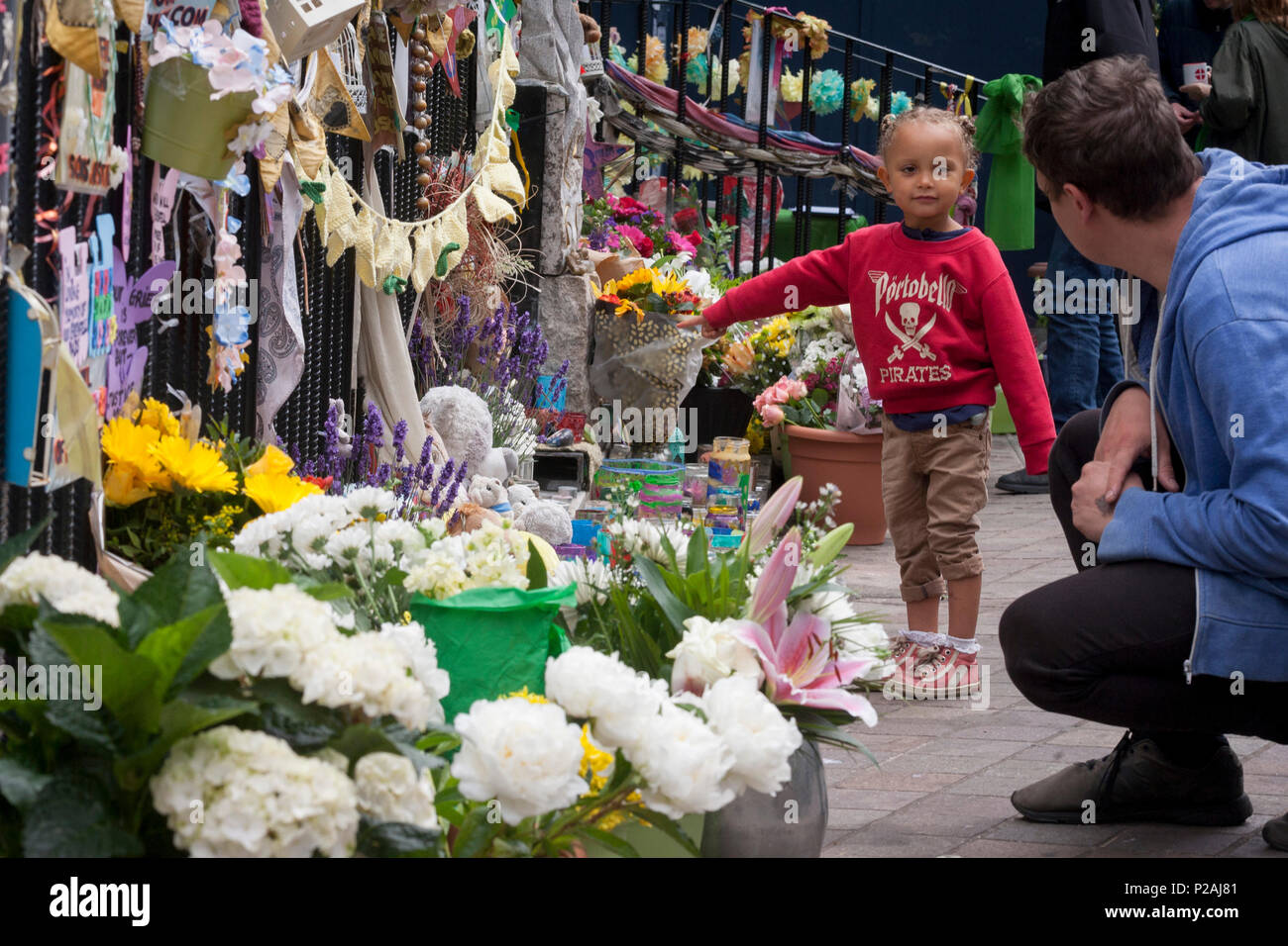 London, UK. 14th Jun, 2018.  A young child looks at flowers left near where the Grenfell fire occured, on the first anniversary of the tower block disaster. 72 people died when the tower block in the borough of Kensington & Chelsea were killed in what has been called the largest fire since WW2. The 24-storey Grenfell Tower block of public housing flats in North Kensington, West London, United Kingdom. It caused 72 deaths, out of the 293 people in the building, including 2 who escaped and died in hospital. Over 70 were injured and left traumatised. Credit: RichardBaker/Alamy Live News Stock Photo