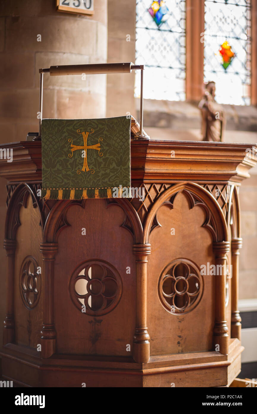 Church interior: close up of traditional C of E pulpit with decorative wooden panels & embroidered cloth parament (cross symbol) hanging from lectern. Stock Photo