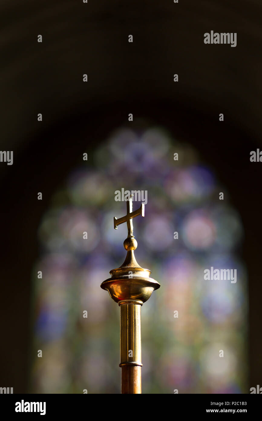 Close up of isolated brass cross with stained glass window in background. Church interior of Christian faith, traditional C of E. Stock Photo