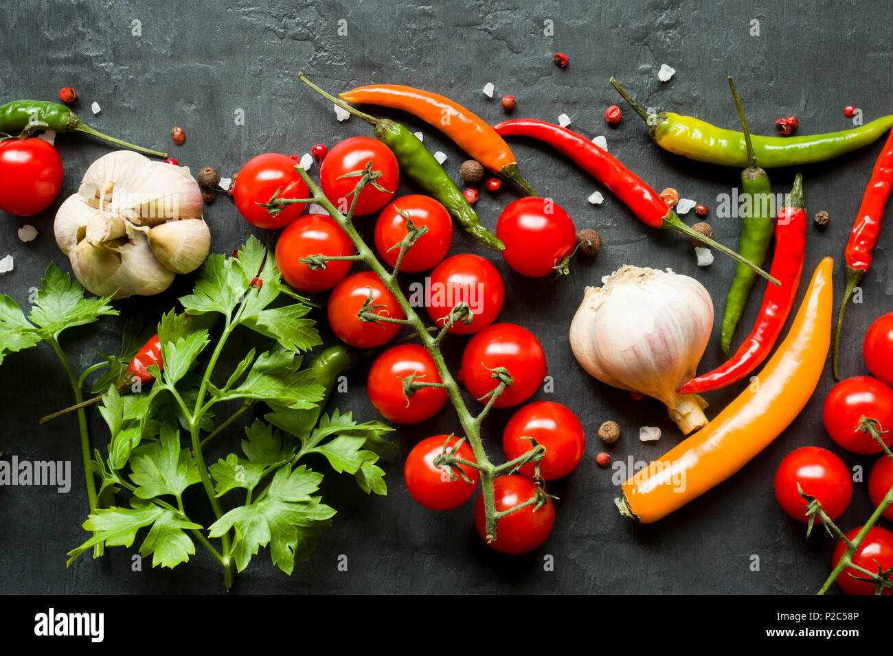 Hot chili peppers multi-colored, tomato cherry on branch, garlic and other spices on black background. Stock Photo