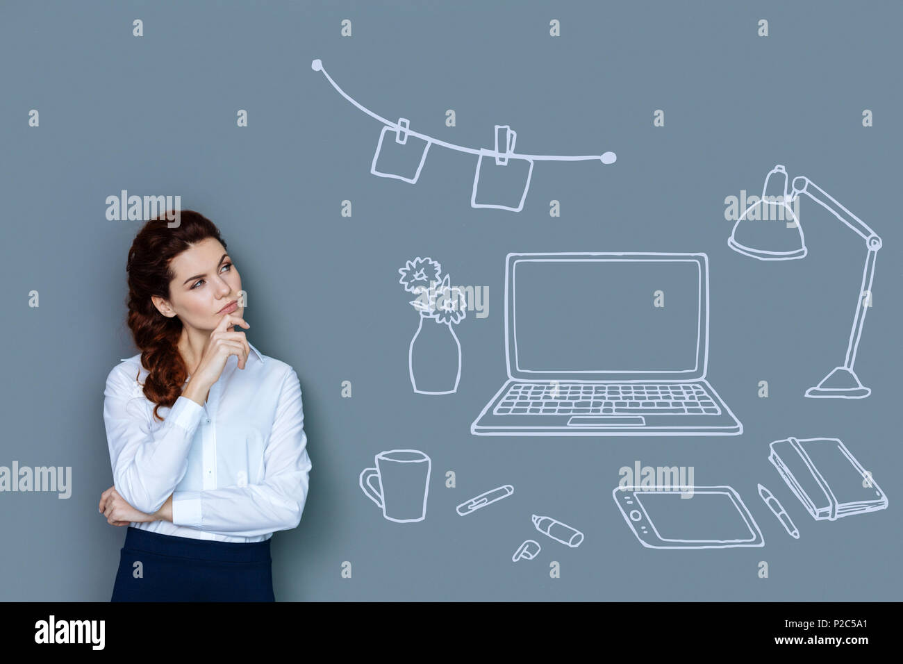 Calm secretary thoughtfully touching her chin and looking at the working place Stock Photo