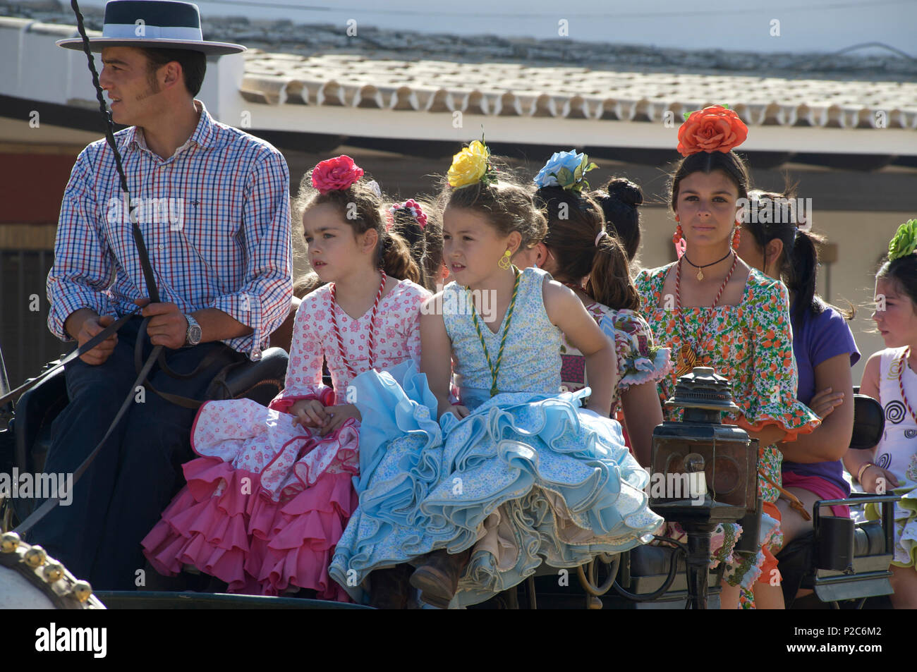 Girls and young woman in q horse carriage in Flamenco dresses, Pilgrims in front of the church at El Rocio at Pentecost, Huelva, Stock Photo