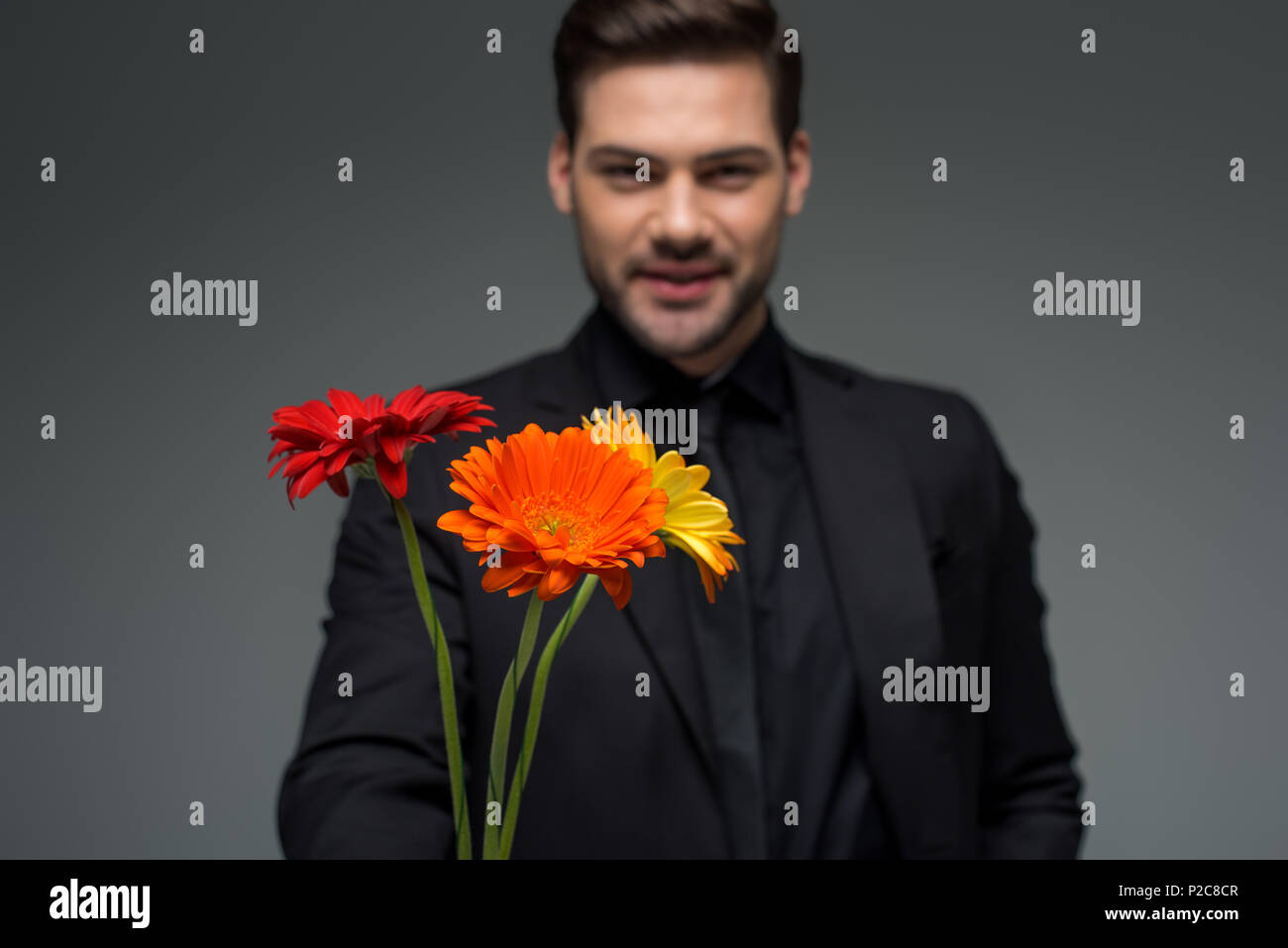 Smiling male with bouquet of flowers isolated on grey, international womens day concept Stock Photo