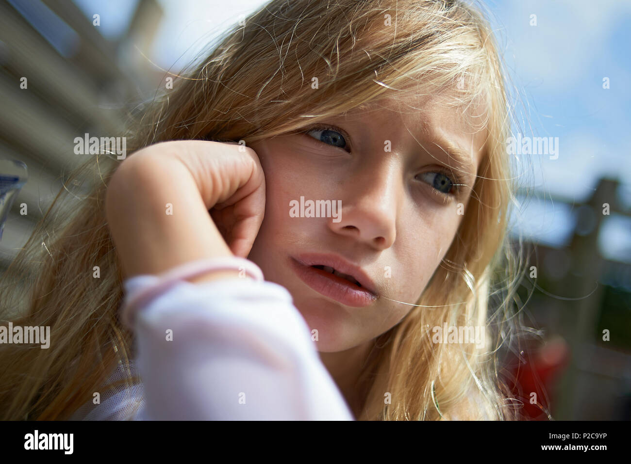 Portrait fo a young preteen blonde girl sitting outside with her head in her hands looking upset and sulky Stock Photo