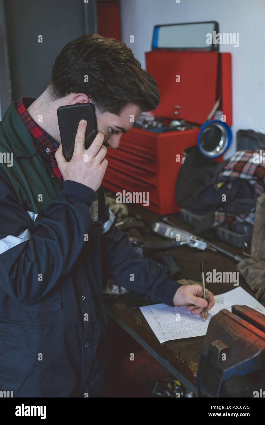 Mechanic writing on paper while talking on a mobile phone Stock Photo