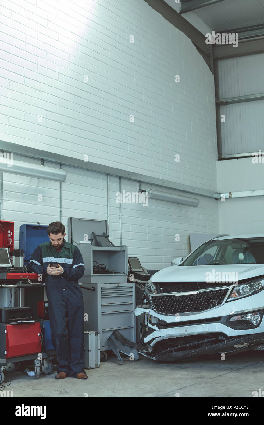 Mechanic using mobile phone while repairing car Stock Photo