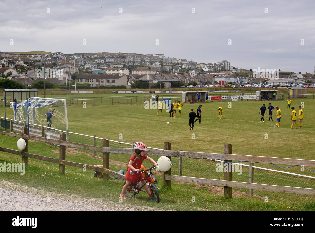 A girl cycles past a football match between Perranporth and Threemilestone at Perranporth, Cornwall. Stock Photo