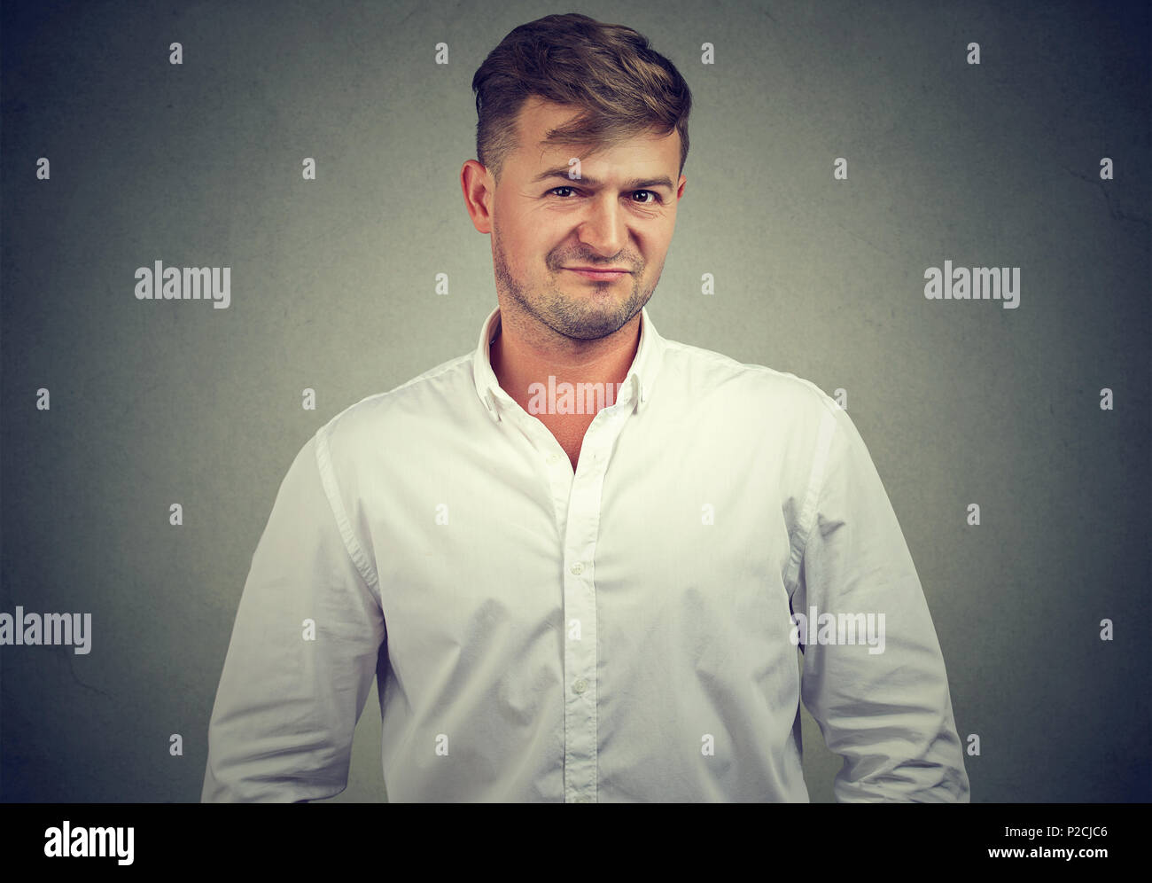Young man in white shirt frowning at camera looking full of skepticism and mistrust on gray background Stock Photo
