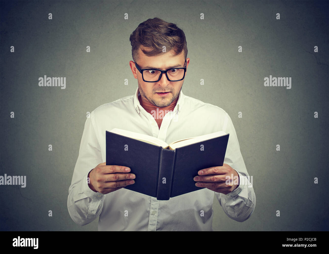 Man in glasses holding textbook and reading information with gasp looking super excited with news Stock Photo