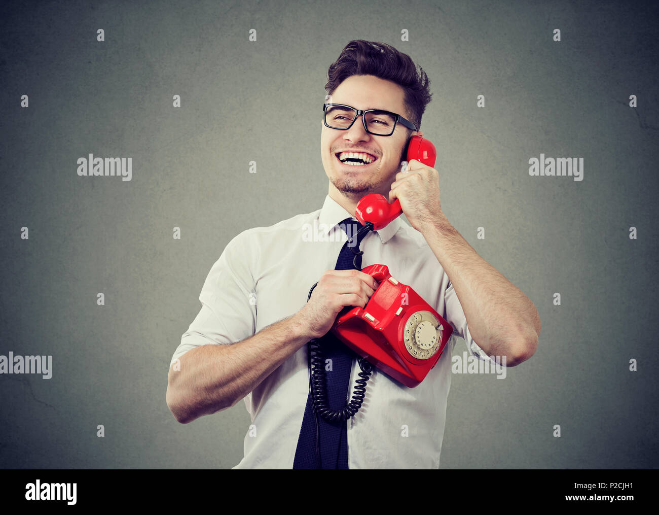 Happy young man speaking on retro phone and laughing looking happy with good news. Stock Photo