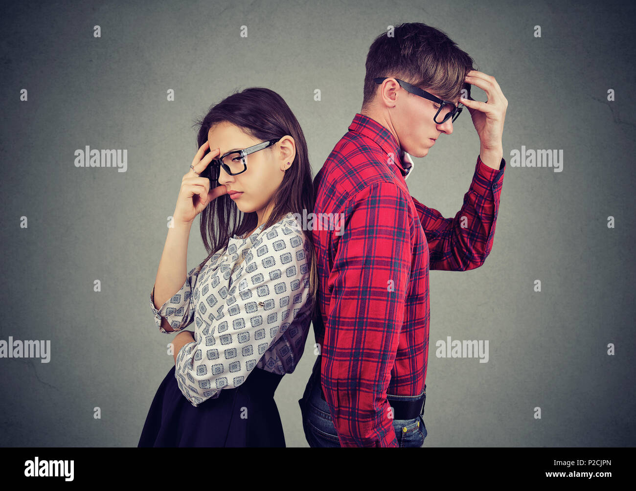 Young stressed couple with hand on head standing back to back looking down in frustration Stock Photo