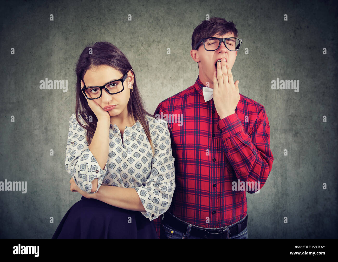 Man and woman on date both looking dull and disinterested standing on gray backdrop. Stock Photo
