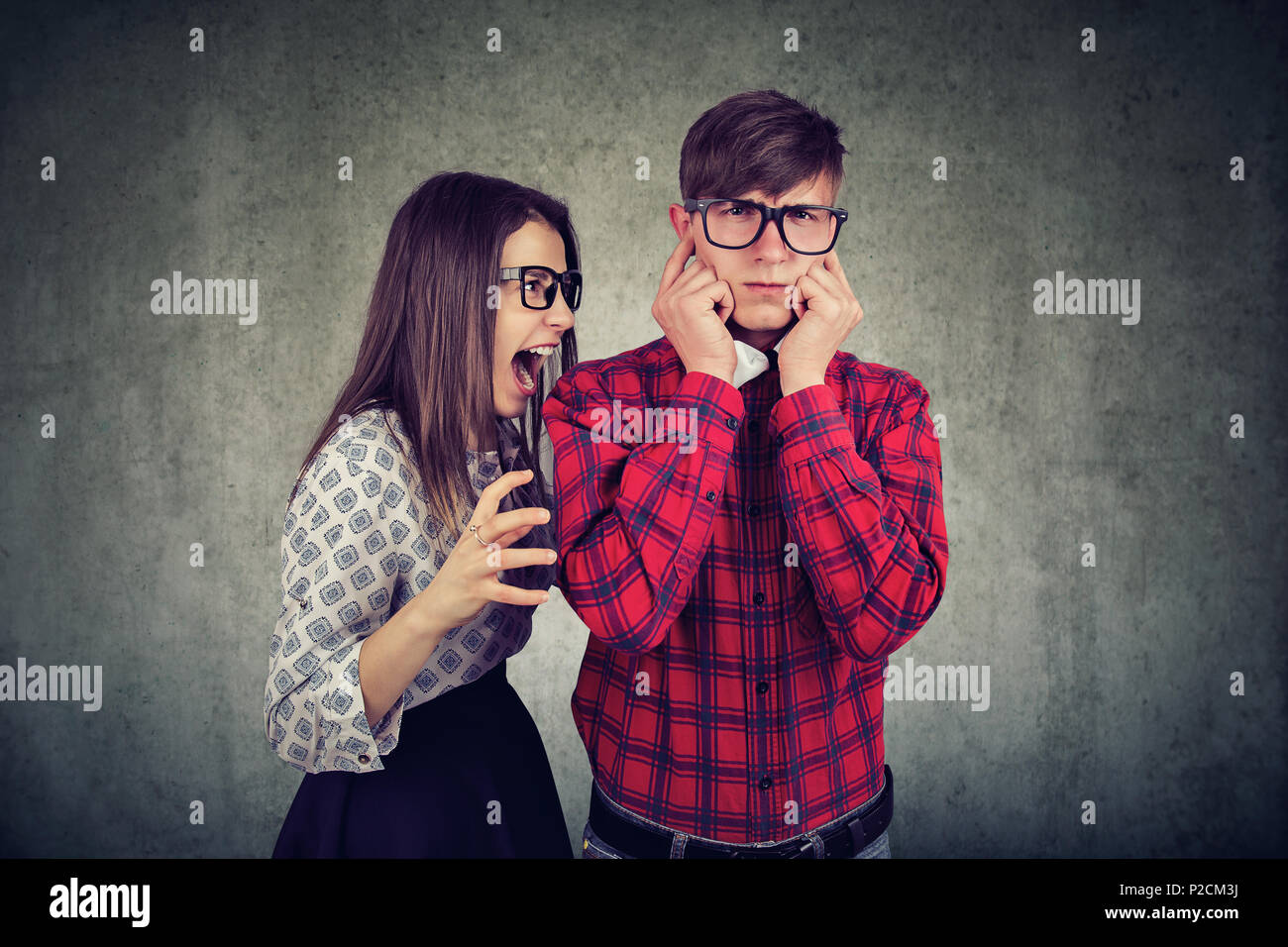 Woman screaming at man having big scandal while he covering ears in disagreement on gray backdrop. Stock Photo