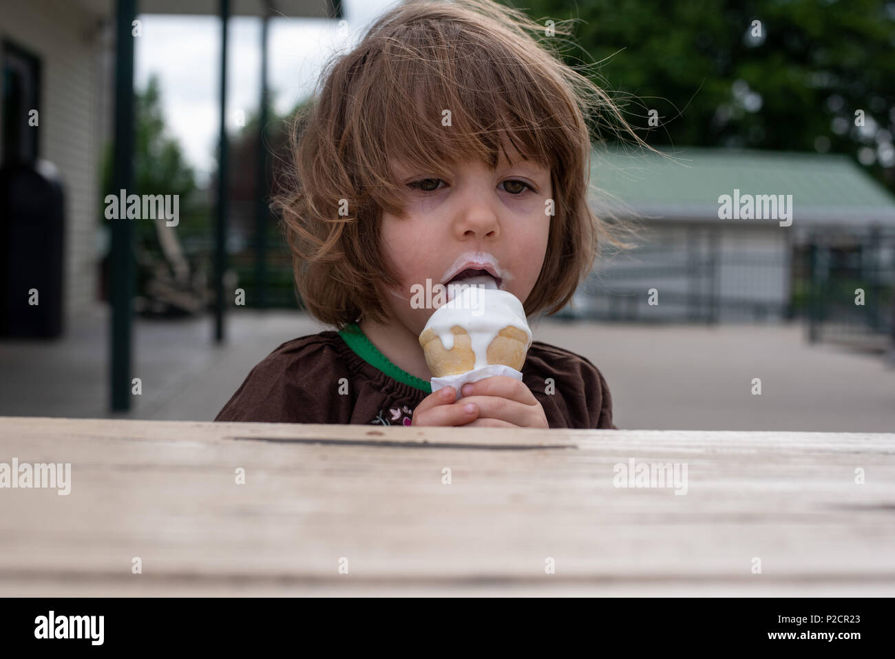 A preschool girl eats an ice cream cone at an ice cream stand in the