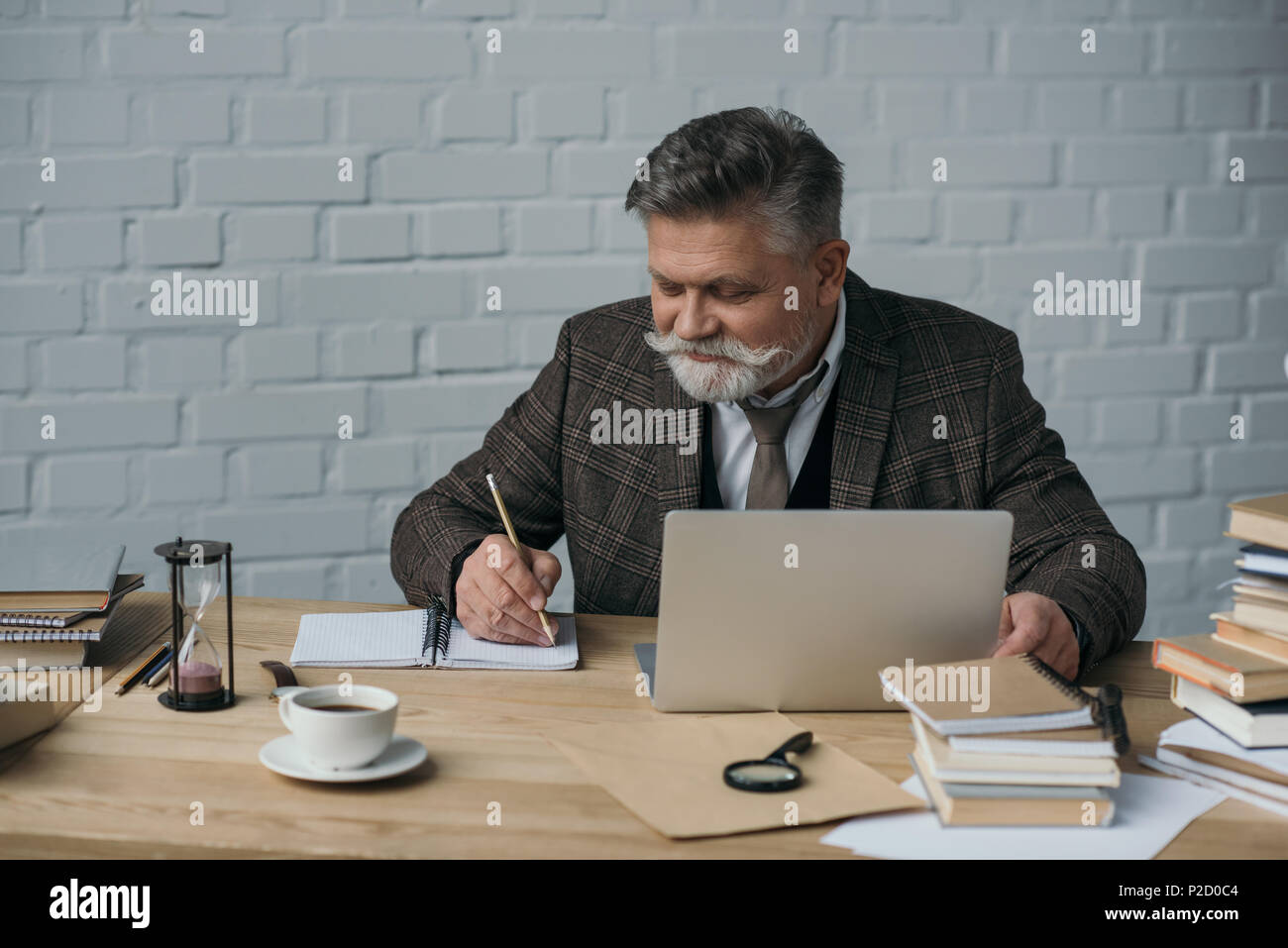 happy senior writer working with laptop and making notes in notebook Stock Photo