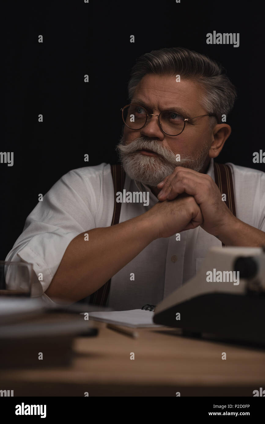 thoughtful senior writer sitting at workplace and looking away isolated ...