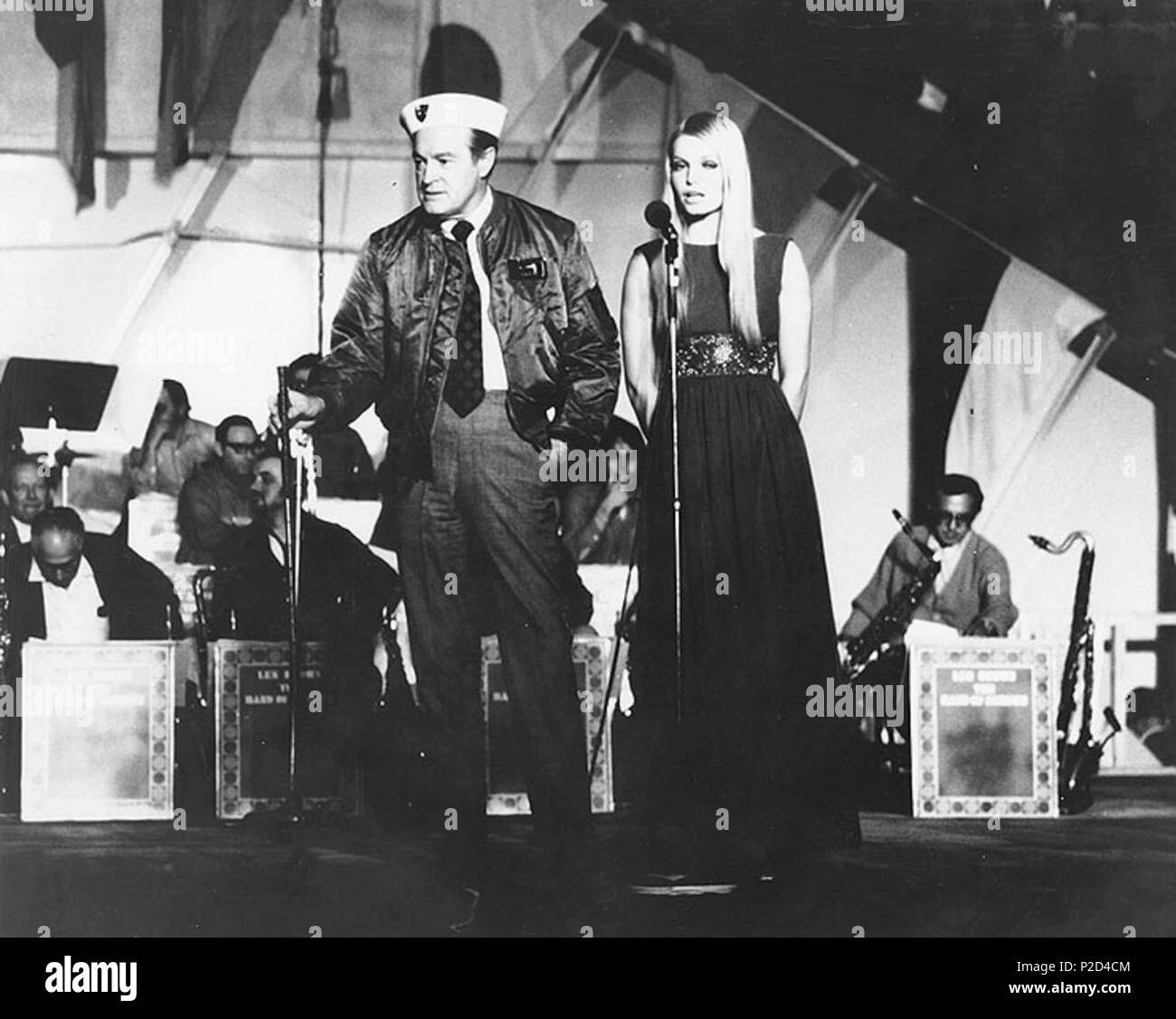 . The entertainer Bob Hope on stage with Miss World 1969, Eva Rueber-Staier, during a Christmas show for servicemen held on board the U.S. Navy aircraft carrier USS Saratoga (CVA-60), off Gaeta, in Formia Bay, Italy, 22 December 1969. The Bob Hope USO Tour performed at 1400 hrs. aboard Saratoga with Eva Rueber-Staier, Hollywood stars Connie Stevens, Suzanne Charny, the 'Golddiggers', Ellen Farley, and Les Brown and his 'Band of Renown'. Over 6.000 Sixth Fleet sailors from Saratoga, USS Little Rock (CLG-4), five destroyers and a fleet oiler attended the event held in the carrier's hanger bay. 2 Stock Photo