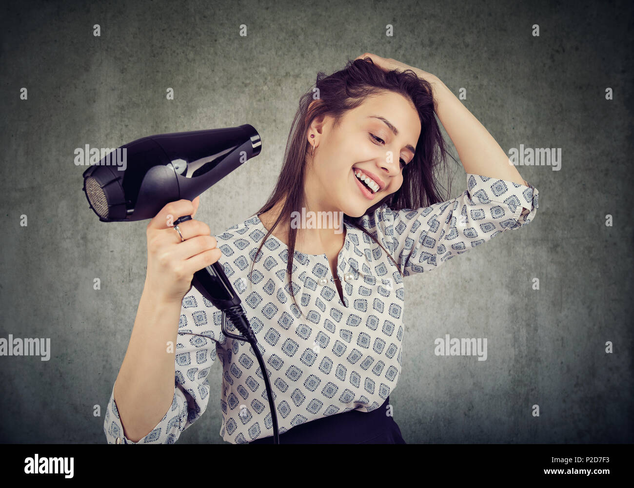 Smiling young woman drying her hair with a hairdryer Stock Photo - Alamy