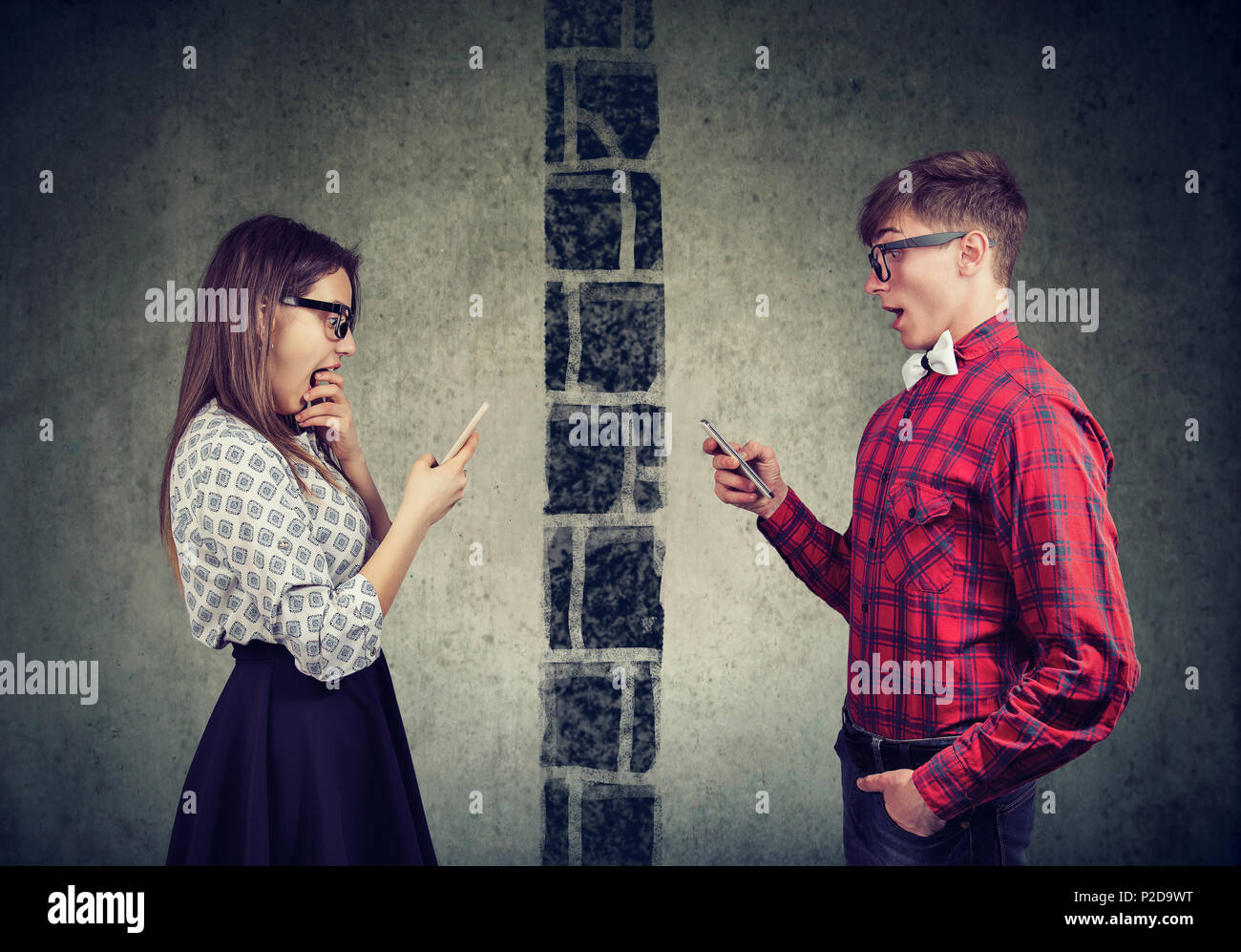 Shocked young couple man and woman separated by wall texting each other on mobile phone Stock Photo