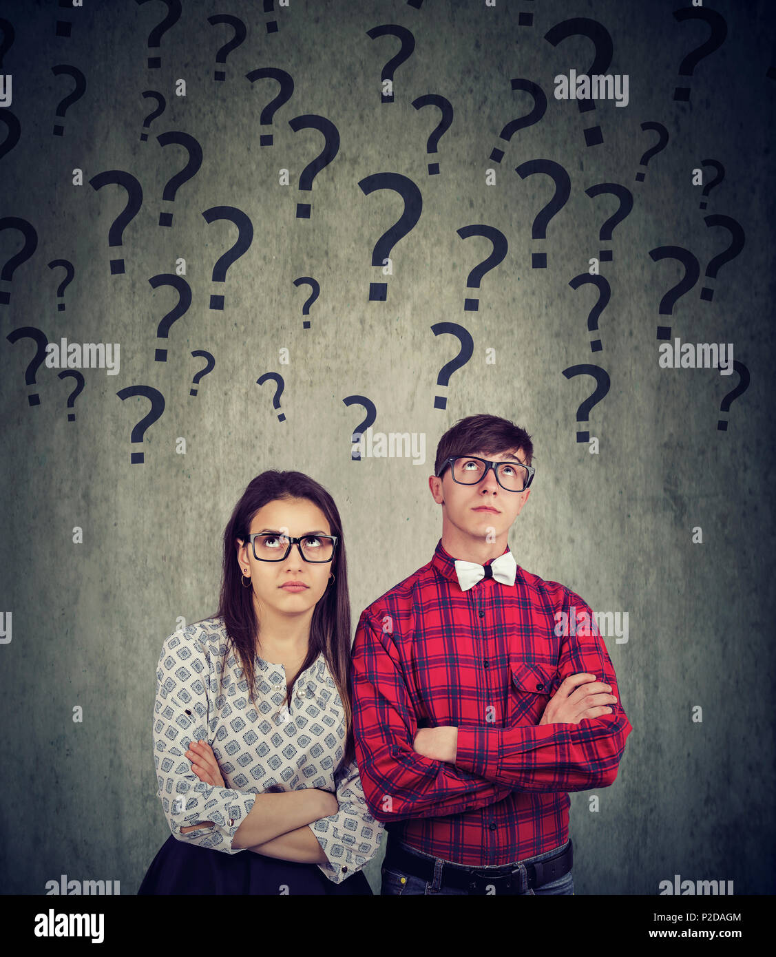 Young man and woman in glasses standing with hands crossed and looking up having problems and questions. Stock Photo