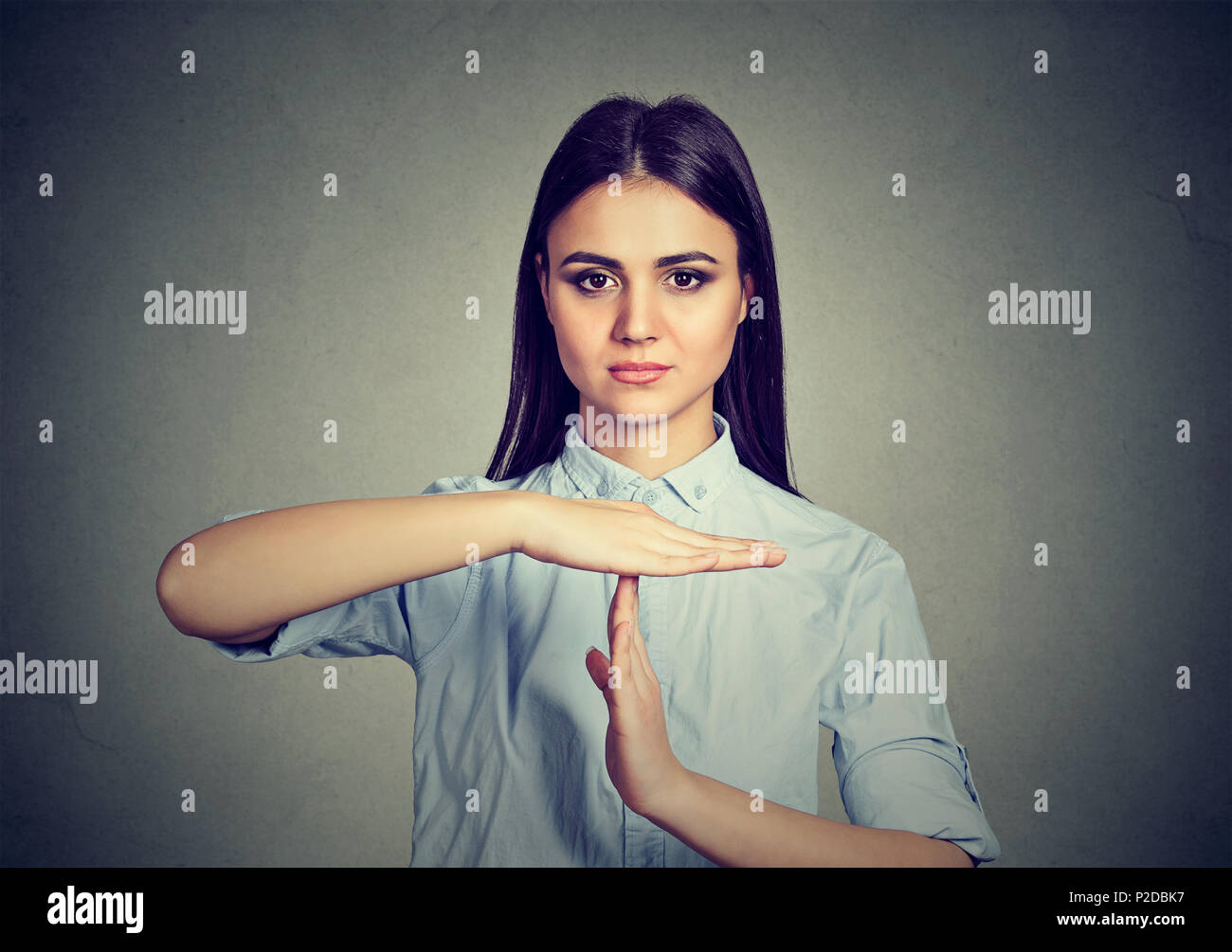 Young serious brunette gesturing for timeout looking at camera confidently while negotiating on gray Stock Photo