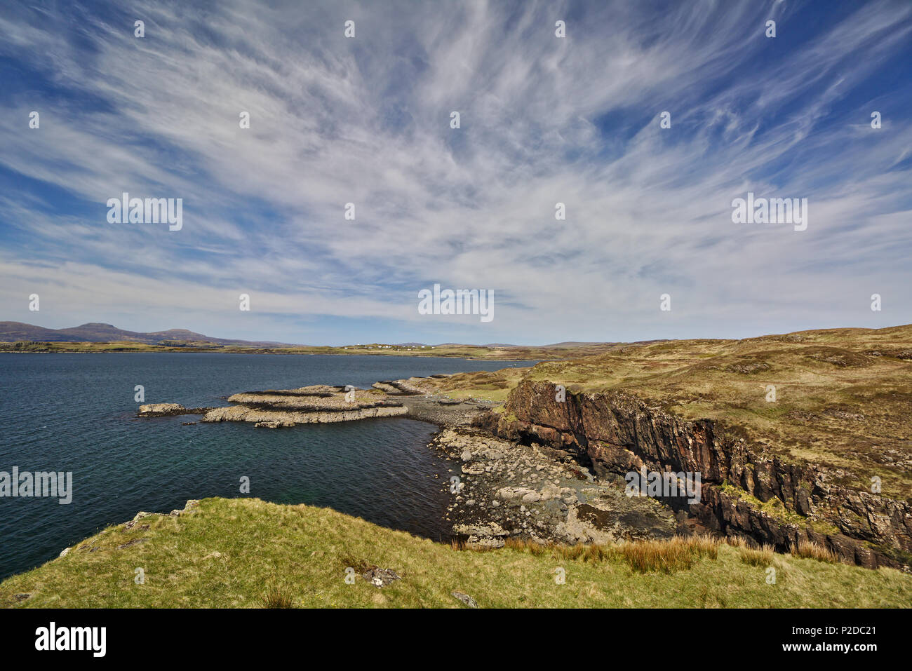 Sea cliff with low headland in the background and blue sky with white cirrus clouds Stock Photo