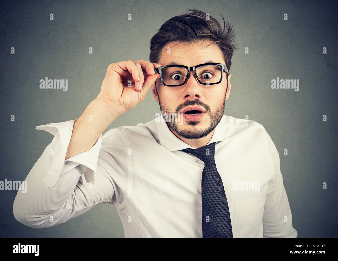 Young bearded man in shirt looking through glasses with amazement and disbelief on gray background Stock Photo