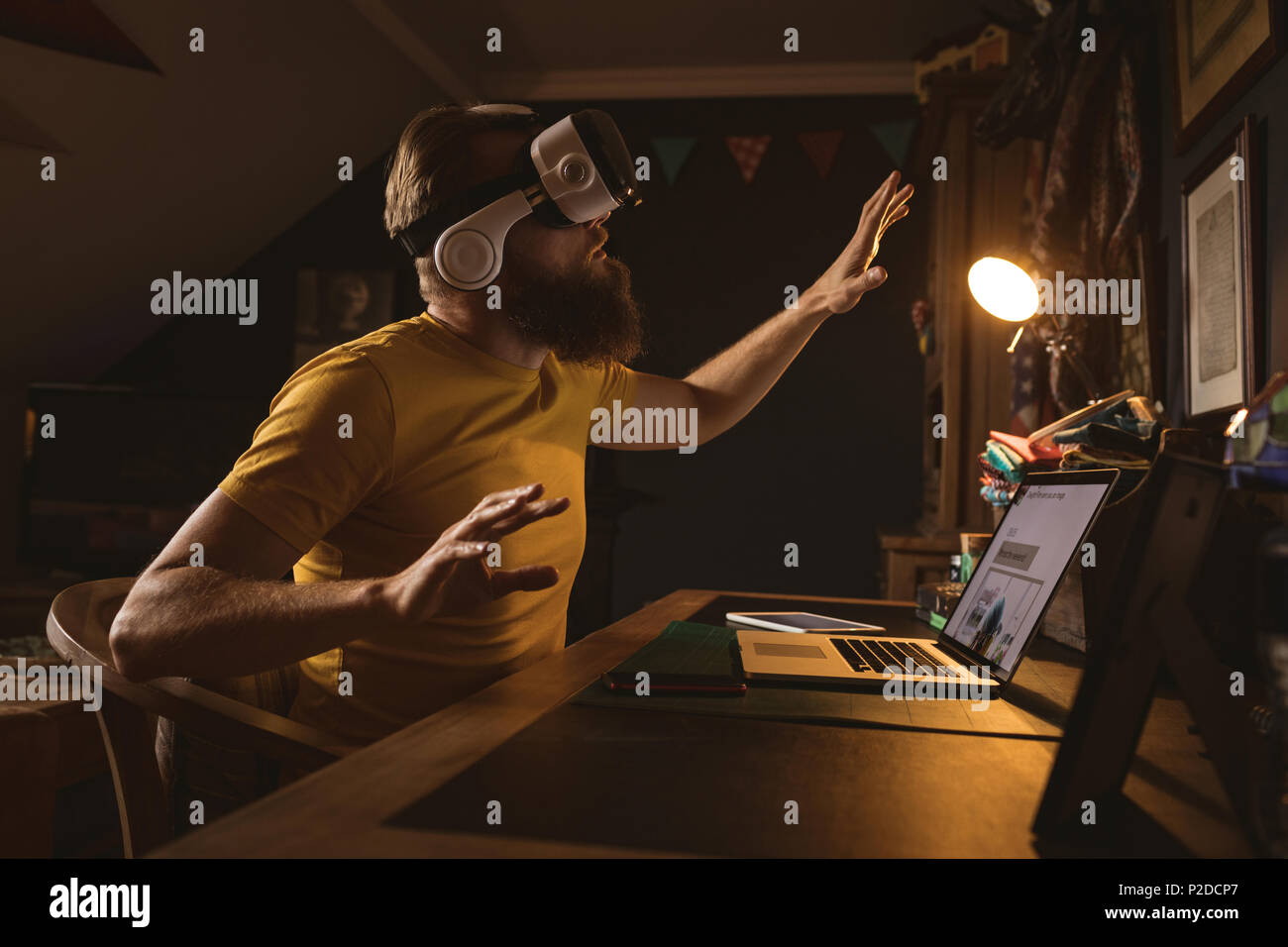 Man wearing virtual reality headset sitting front of laptop Stock Photo