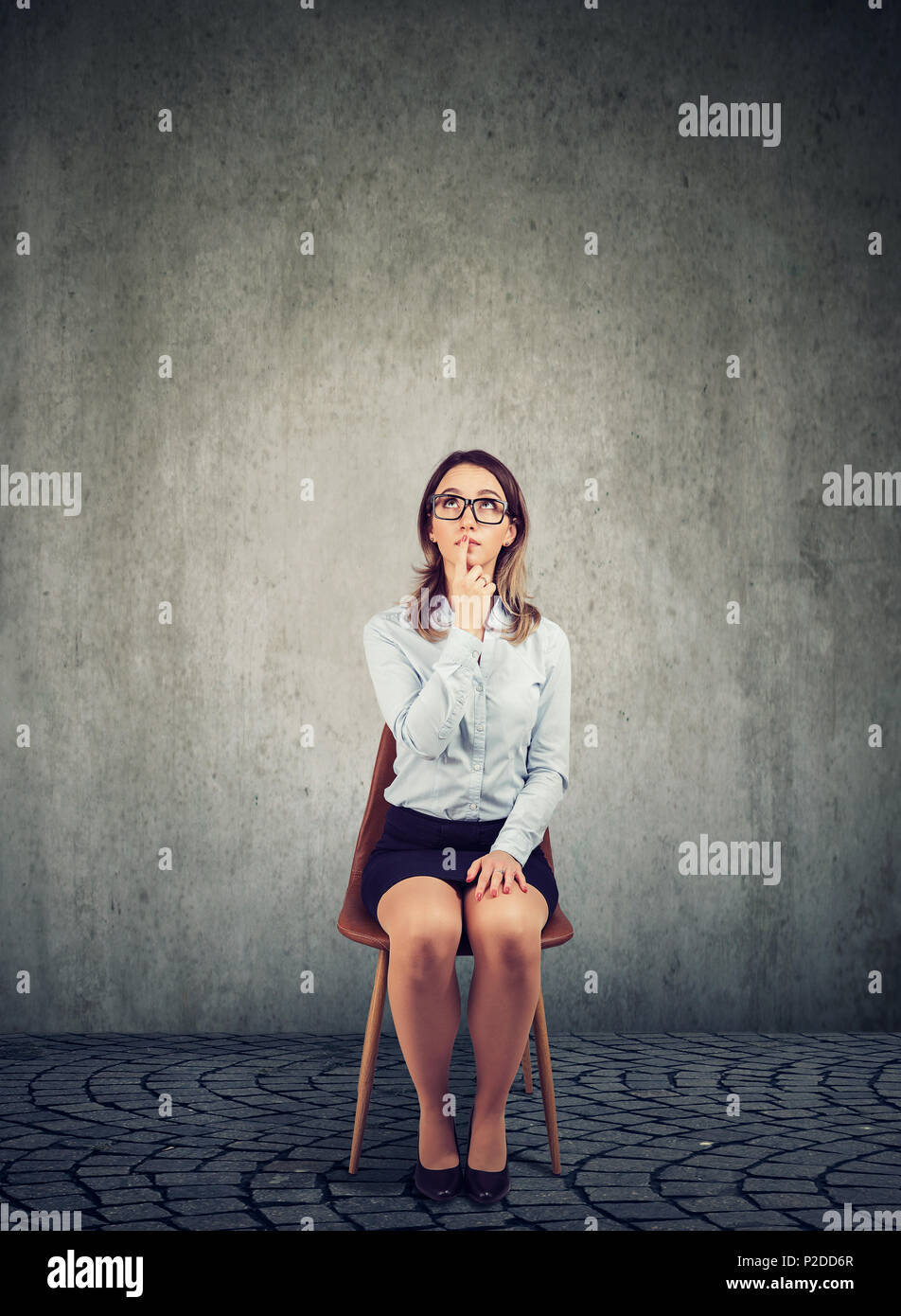Pensive business woman sitting on chair and contemplating on plan against gray background Stock Photo