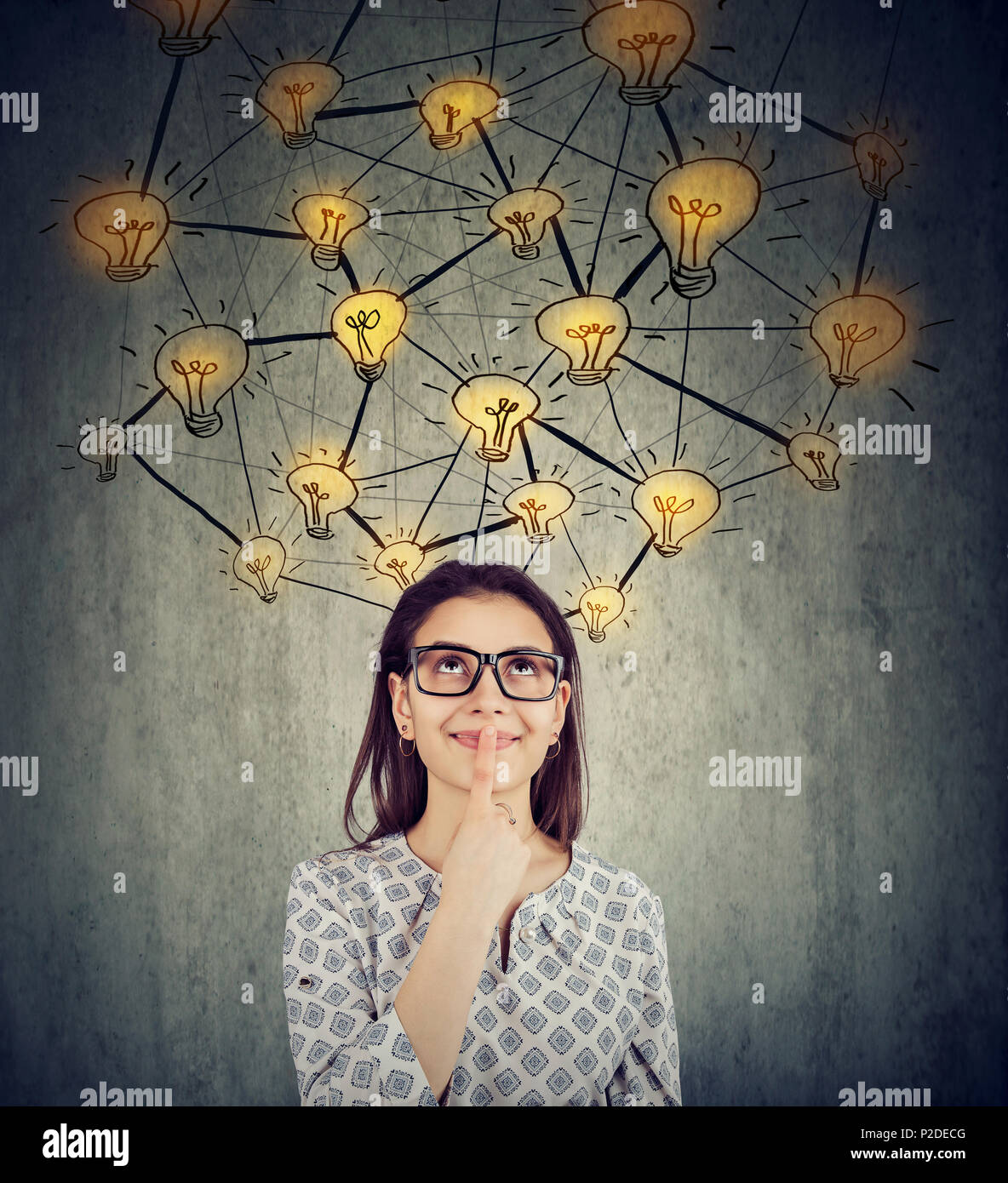 Cute woman in glasses with many ideas light bulbs above head looking up isolated on wall background. Stock Photo