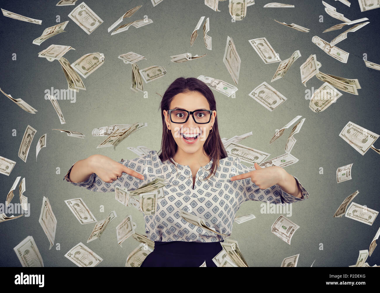 Portrait of an excited happy woman pointing fingers at herself in disbelief of being a winner under a money rain falling down dollar bills banknotes Stock Photo