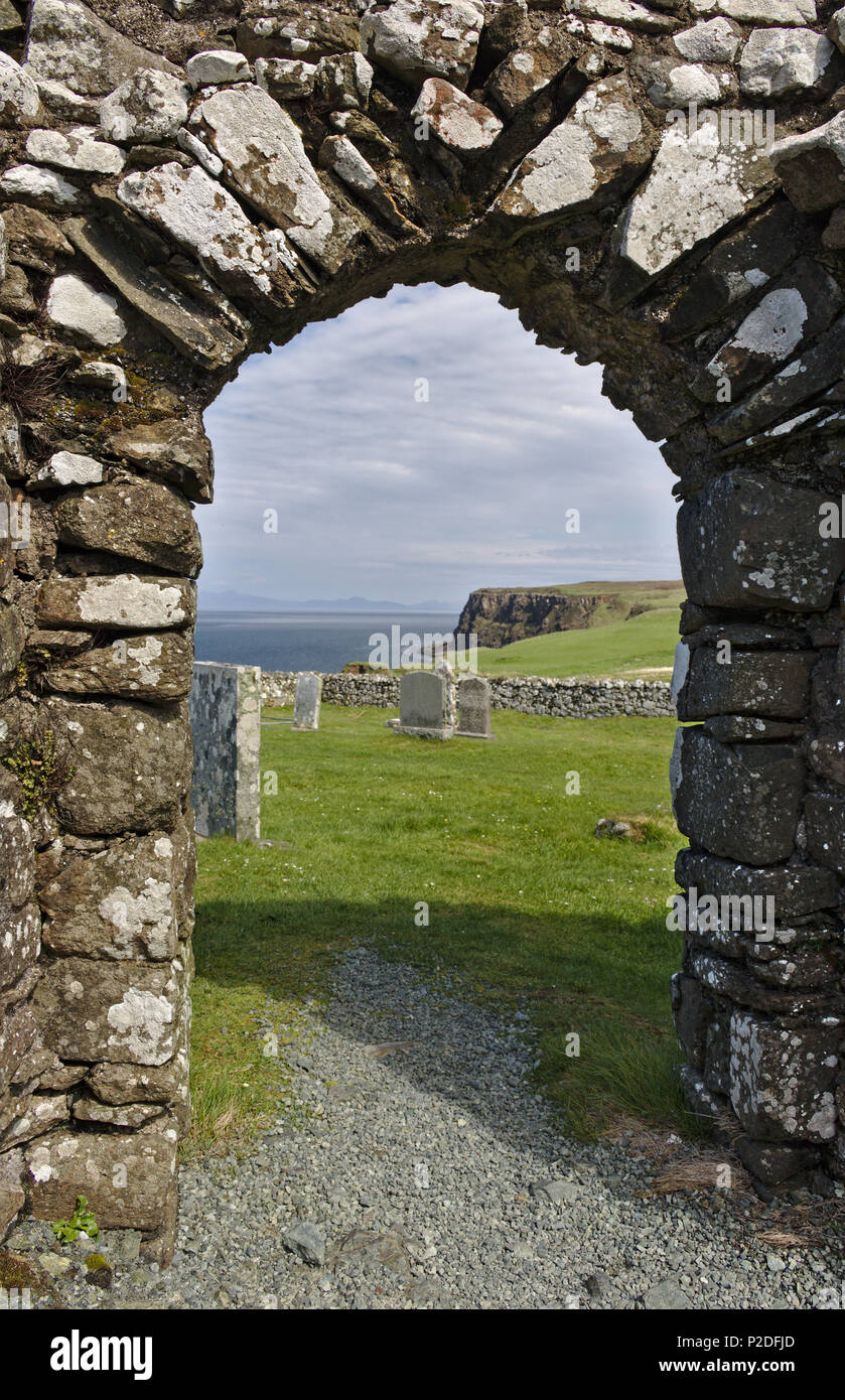Isle of Skye, Scotland - View through the archway of ruined Trumpan church across a green grassy graveyard towards a distant sea cliff Stock Photo