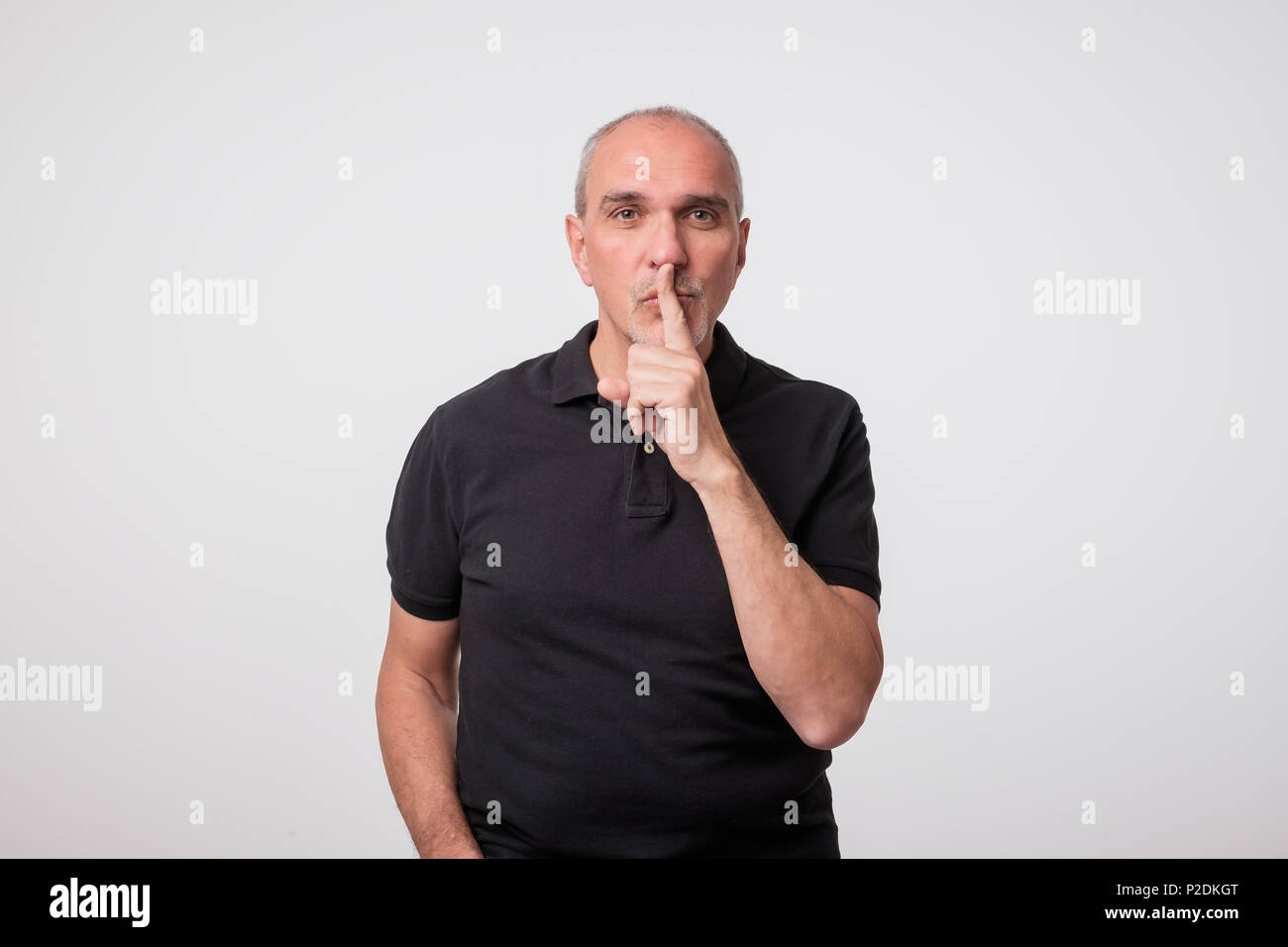 handsome old man in black t-shirt with finger on his lips. Stock Photo
