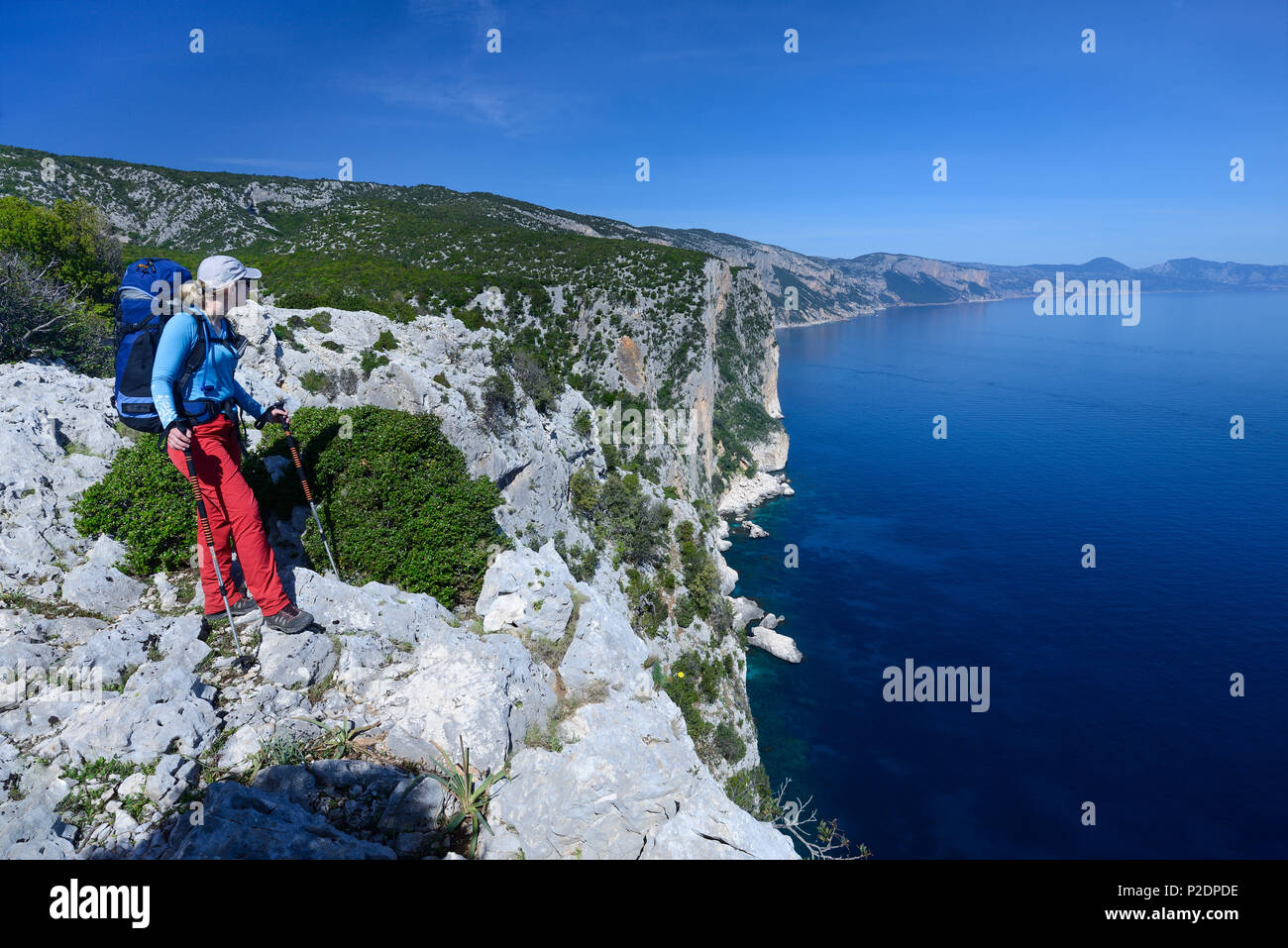 A young woman with trekking gear hiking along the mountainous coast above the sea, Selvaggio Blu, Sardinia, Italy, Europe Stock Photo