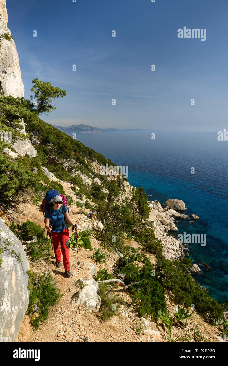 A young woman with trekking gear hiking along the mountainous coast above the sea, Golfo di Orosei, Selvaggio Blu, Sardinia, Ita Stock Photo