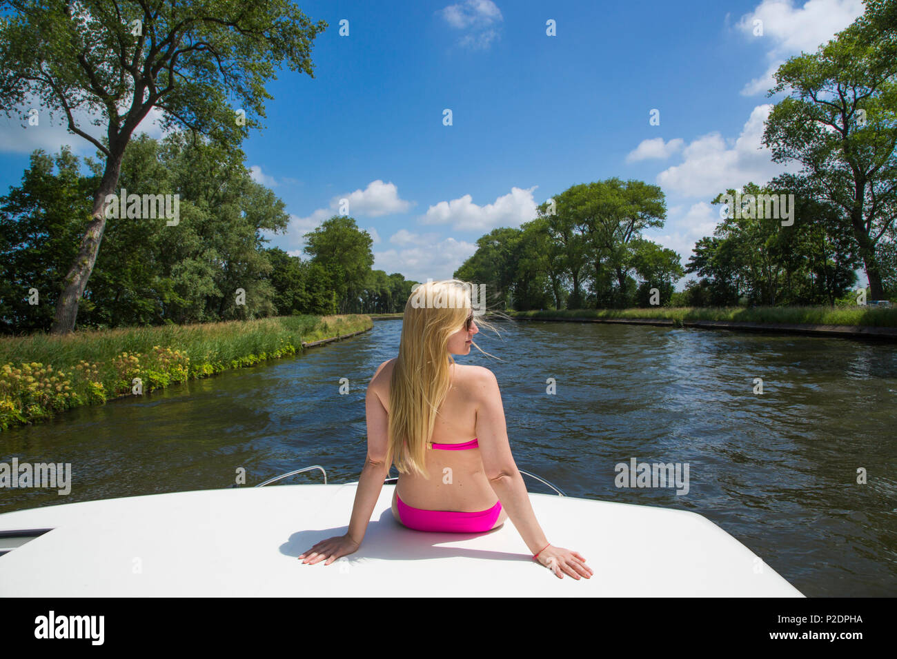 Young blonde woman wearing a bikini relaxes on deck of a Le Boat Royal Mystique houseboat on the Plassendale - Niuewpoort canal, Stock Photo