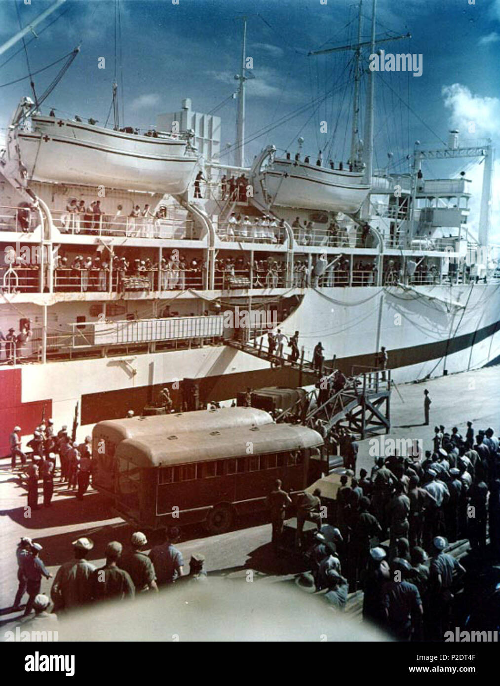 . Survivors of the heavy cruiser USS Indianapolis (CA-35) are brought ashore from the U.S. Navy hospital ship USS Tranquillity (AH-14) at Guam, 8 August 1945. Nurses and sailors are watching from the hospital ship's deck. Note Tranquillity's nested lifeboats and the busses on the pier. 8 August 1945. USN 61 Survivors of USS Indianapolis (CA-35) arrive at Guam in August 1945 Stock Photo