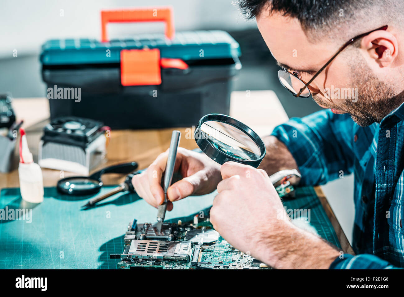 Hardware engineer looking at circuit board through magnifying glass