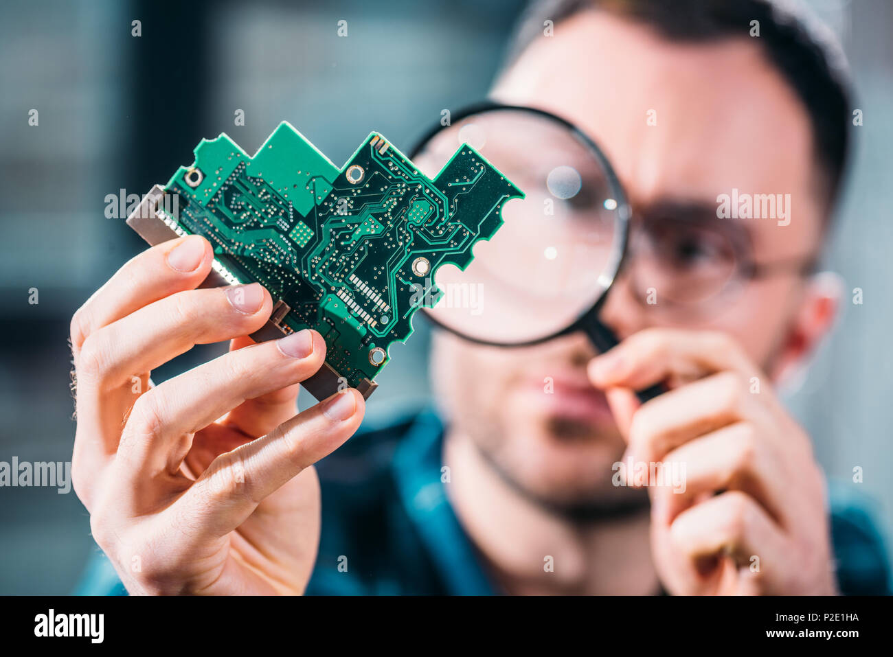 Close-up view of man looking at circuit board through magnifying glass ...