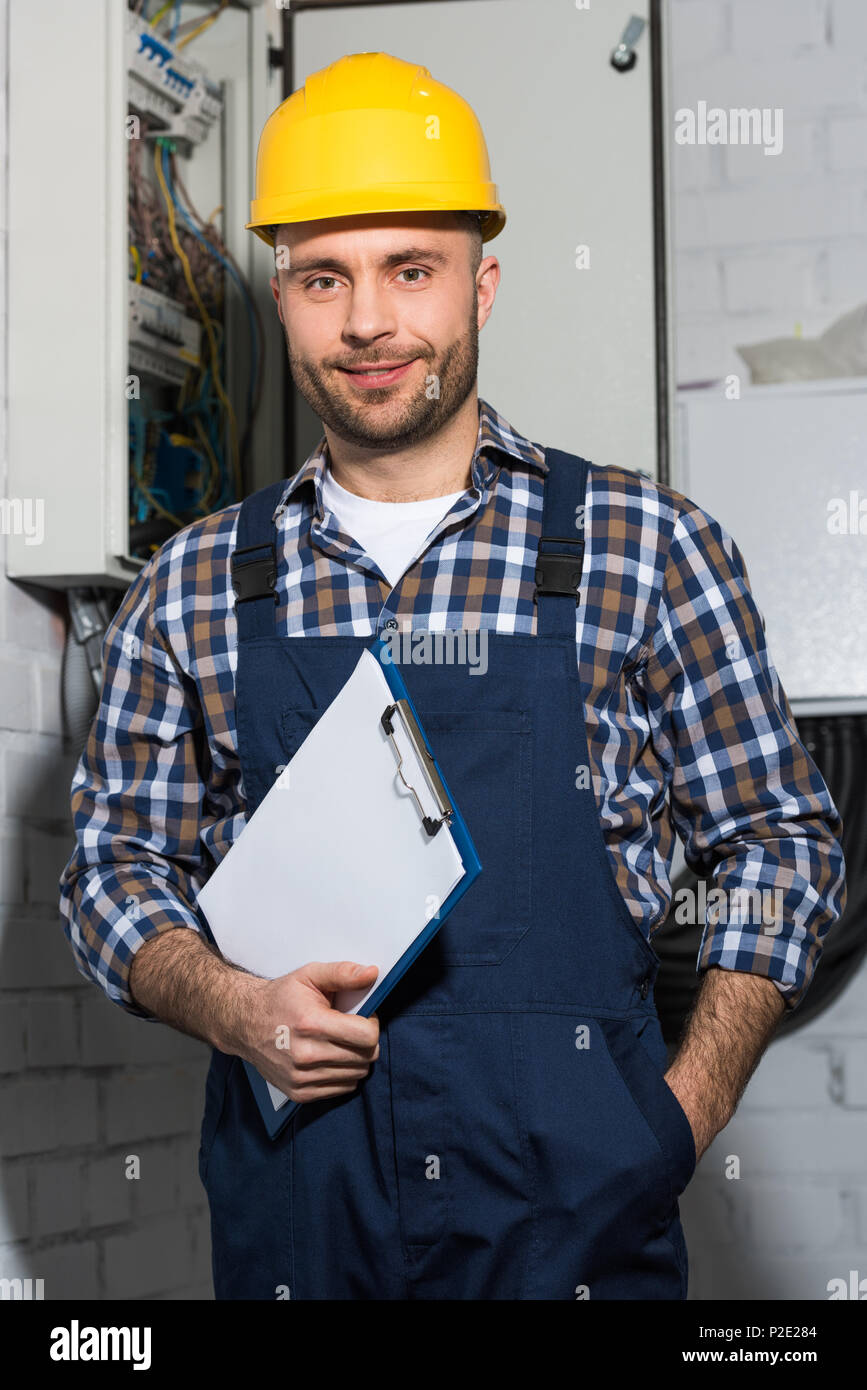 Electrician holding clipboard and smiling by electrical box Stock Photo