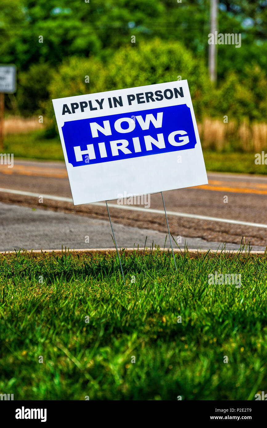 Vertical close-up shot of a Now Hiring Sign with copy space.  Background is out of focus. Stock Photo