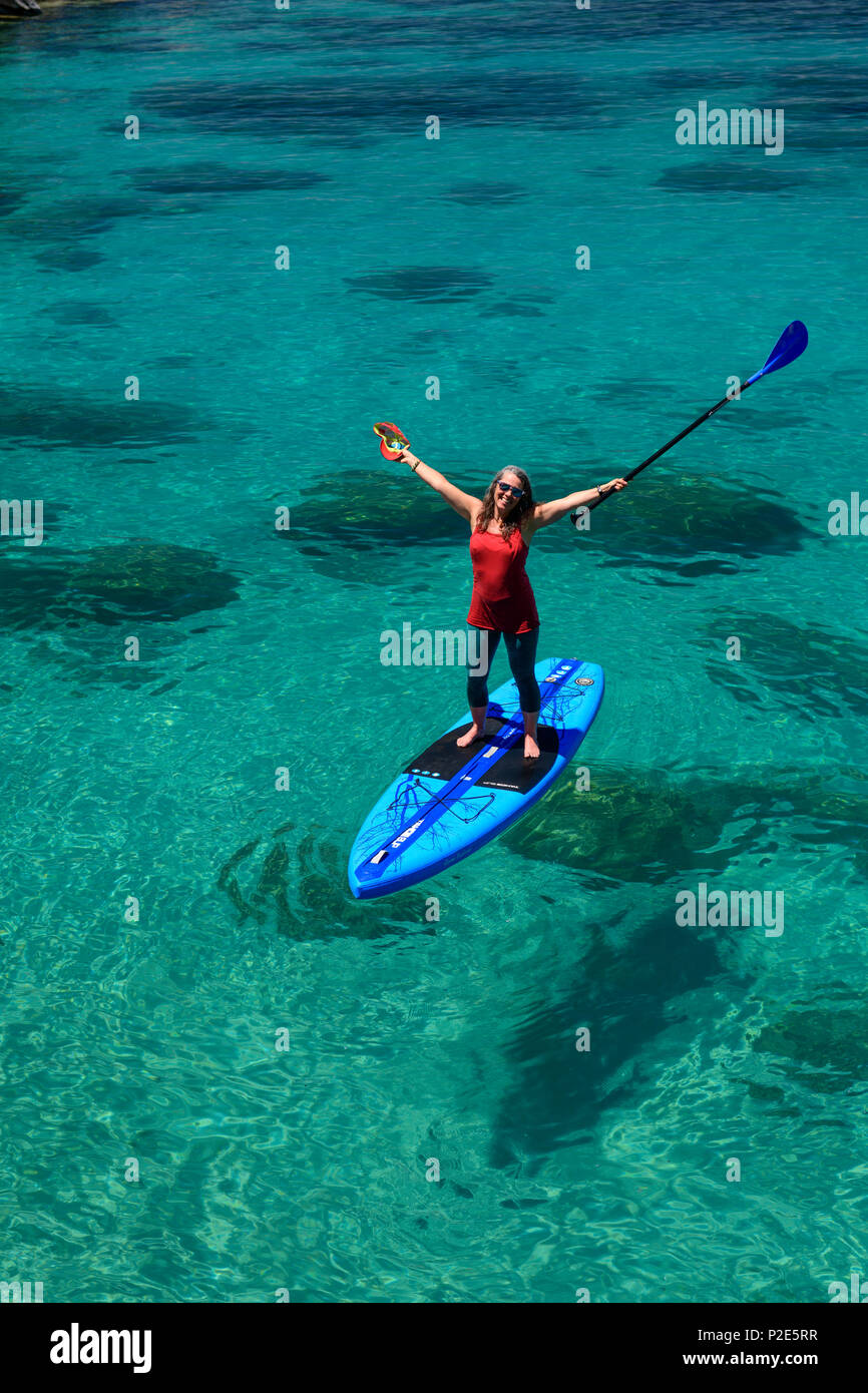 Woman stand up paddle boarding on the crystal clear blue waters of Lake