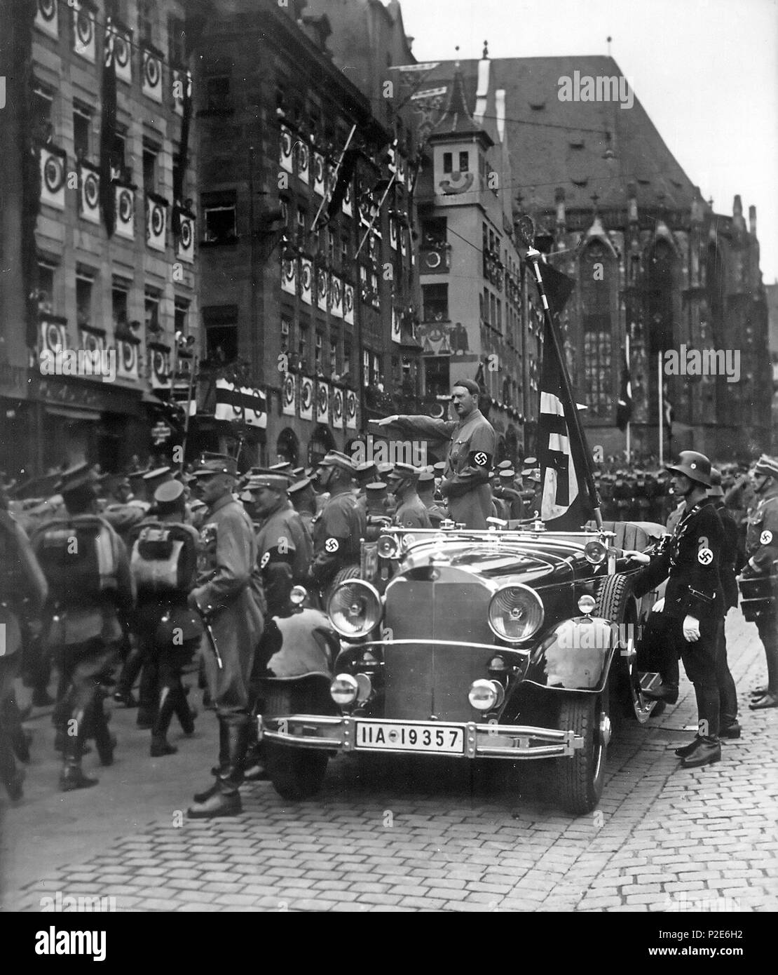. English: Parade of SA troops past Hitler, Nuremberg 1935. In the car with Hitler: the Blutfahne, behind the car: SS-man en:Jakob Grimminger the carrier of the Blutfahne flag. From the Reichsparteitag der NSDAP 10th-16th September 1935 (see also File:Bundesarchiv Bild 183-1982-0809-502, Nürnberg, Reichsparteitag, SA-Marsch.jpg Deutsch: Nürnberg, eine Parade der SA marschieren an Hitler vorbei. Im Auto hinter Hitler: Die de:Blutfahne (NSDAP), rechts daneben der SS-Mann de:Jakob Grimminger, der Träger der Blutfahne war . September 1935. This file is lacking author information. 45 Reichsparteita Stock Photo