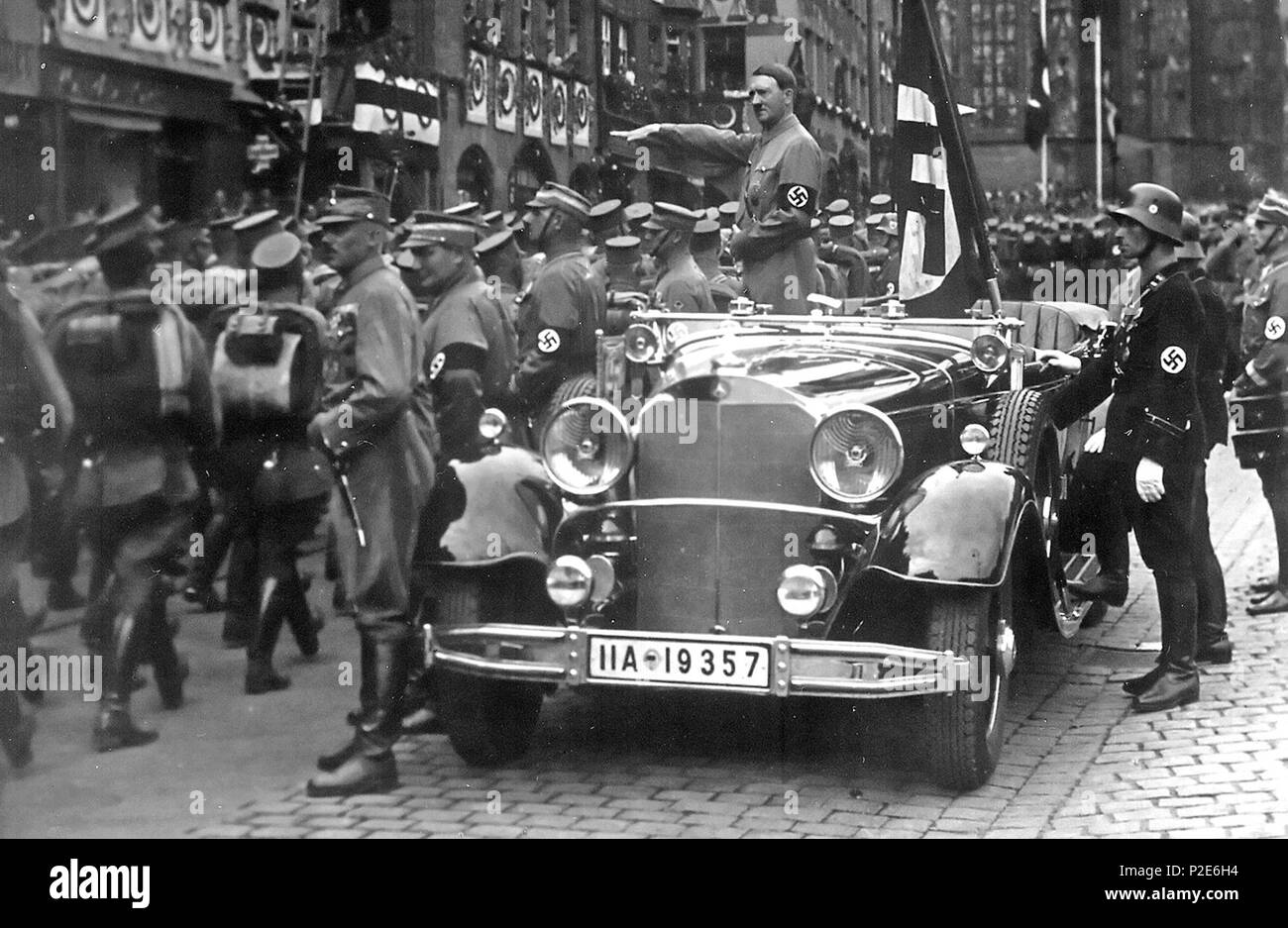 . English: Parade of SA troops past Hitler, Nuremberg 1935. In the car with Hitler: the Blutfahne, behind the car: SS-man en:Jakob Grimminger the carrier of the Blutfahne flag. From the Reichsparteitag der NSDAP 10th-16th September 1935 (see also File:Bundesarchiv Bild 183-1982-0809-502, Nürnberg, Reichsparteitag, SA-Marsch.jpg Deutsch: Nürnberg, eine Parade der SA marschieren an Hitler vorbei. Im Auto hinter Hitler: Die de:Blutfahne (NSDAP), rechts daneben der SS-Mann de:Jakob Grimminger, der Träger der Blutfahne war . September 1935. Charles Russell Collection, NARA. 45 Reichsparteitagnov193 Stock Photo
