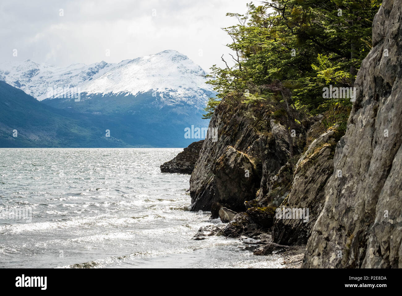 A cliff borders Lake Acigami in the national park of Tierra del Fuego, mountains are on the other side. This lake connects Argentina and Chile. Stock Photo