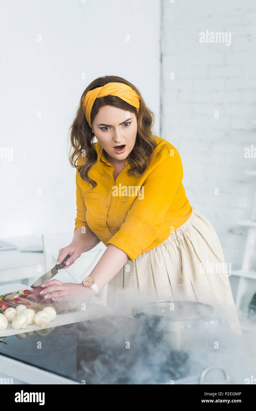 shocked beautiful woman looking at burning pan on electric stove at
