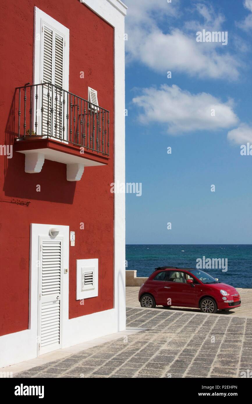 Italy, Puglia, Monopoli, Fiat Cinquecento red parked in front of the sea, at the foot of an old terracotta building Stock Photo